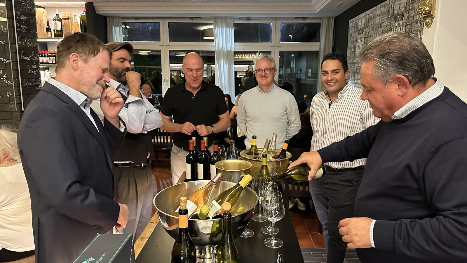 Weinprobe am Stehtisch: Ein Glas wird eingeschenkt, die Runde lacht