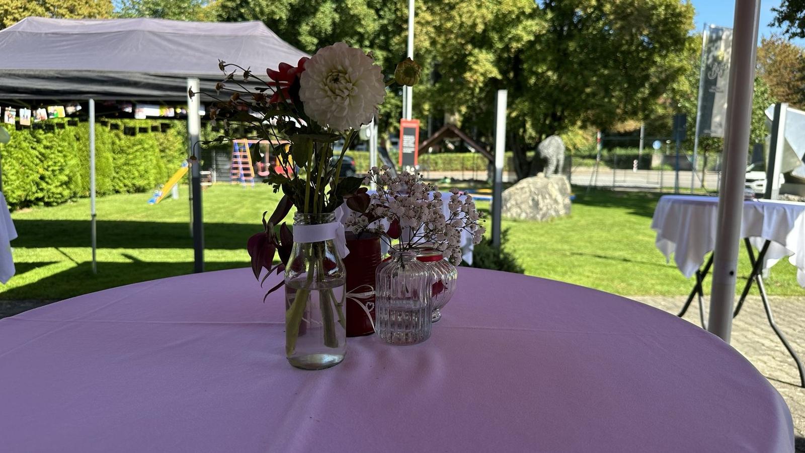 Stehtisch mit Blumen im Garten, im Hintergrund Pavillon und Spielplatz