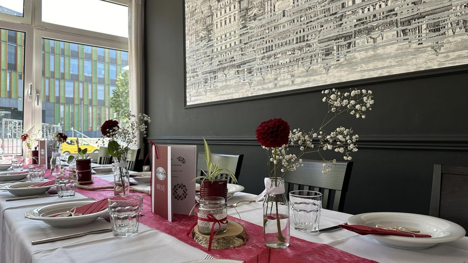 Lange festlich gedeckte Tafel mit rotem Tischläufer, Dahlien und Schleierkraut im Gastraum