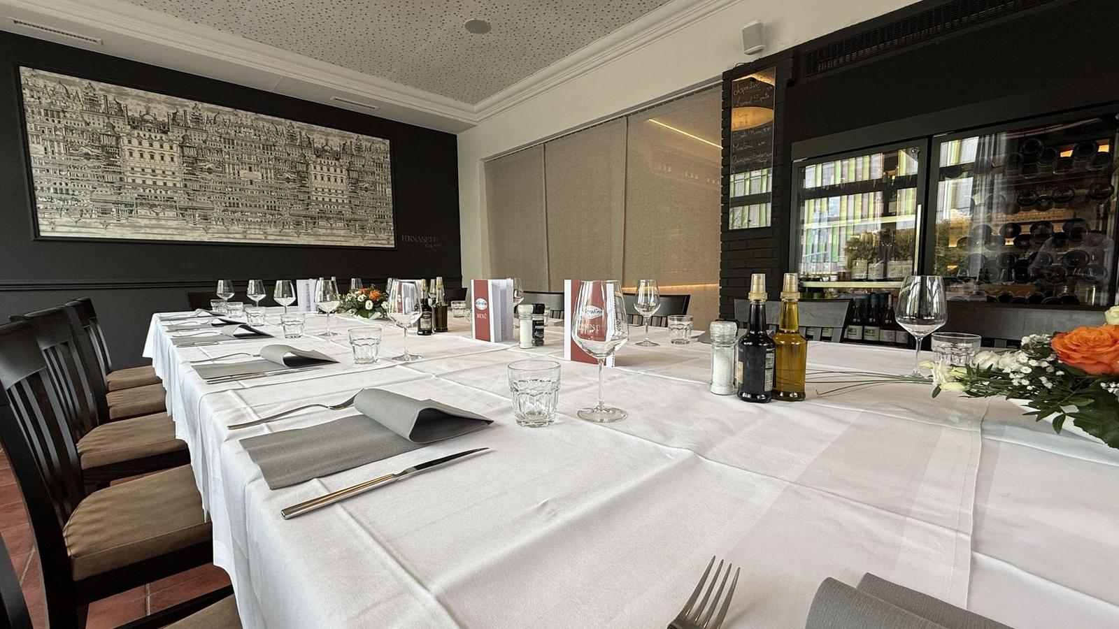 Gedeckter Platz mit Weinglas an der langen Tafel, im Hintergrund der Weinschrank